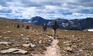 Two hikers follow a rocky trail across an alpine mountain pass
