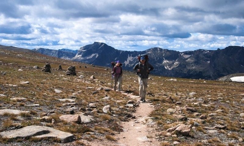 Two hikers follow a rocky trail across an alpine mountain pass