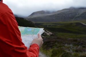 Hiker in a red jacket studies a topographic map in mountain terrain