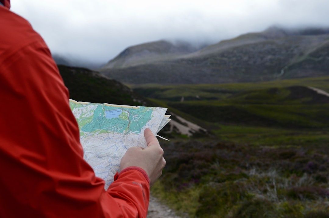 Hiker in a red jacket studies a topographic map in mountain terrain